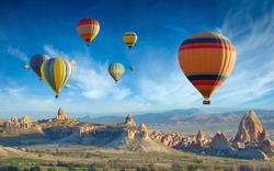 Surise view of unusual rocky landscape in Cappadocia, Turkey. Colorful hot air balloons fly in blue sky over amazing valleys with fairy chimneys in Cappadocia.