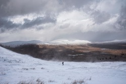 Beautiful Winter landscape image from mountain top in Scottish Highlands down towards Rannoch Moor during snow storm and spindrift off mountain top in high winds