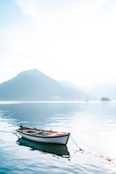 White fishing boat on calm water against the backdrop of mountains in the fog.