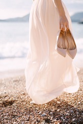 Bride with high-heeled shoes in her hand walks along the beach. Close-up