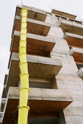 Long yellow pipe stretches up along the balconies of an apartment building under construction