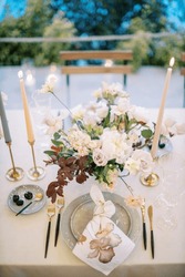 Lighted candles stand on the table near a bouquet of flowers in front of a plate with a knotted napkin