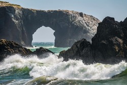 Surf breaking by sea stacks near Arched Rock on a sunny afternoon, Bodega Bay, Sonoma Coast State Park, California, USA, with slight motion blur, for themes of turbulence, erosion, harsh environments