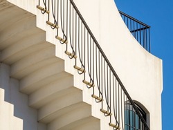Geometric railing and shadowed underside of exterior concrete stairway on sunny side of upscale beach house in New Urbanist architectural style on a bright afternoon along the Gulf Coast of Florida