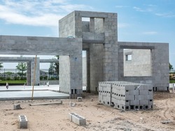 Concrete shell of single-family house under construction, with stacks of concrete blocks near front doorway, in a suburban development on a spring afternoon in southwest Florida