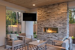 Luxury outdoor relaxing living room with large stone fireplace, TV, rug and beige sofa. 