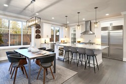 Large bright luxury kitchen interior with large dining room table and island with white marble with dark brown hardwood.