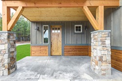 Front covered entrance to a new rustic natural townhome with concrete patio and stone columes.