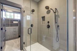Natural new classic slick bathroom interior with new glass walk in shower, white tub and walk in closet.