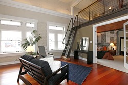 Modern living room with brick painted wall, hardwood floor and iron steep stairs. View of bedroom