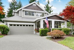 Nice curb appeal of grey house with garage and driveway. Column porch with American flag. Northwest, USA
