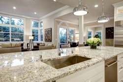 White kitchen design features large bar style kitchen island with granite countertop illuminated by modern pendant lights. Northwest, USA