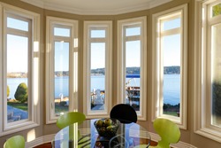 Sun filled breakfast nook features glass top table with black and green chairs atop glossy hardwood floor. Window wall presents picturesque view of Lake Washington. Northwest, USA