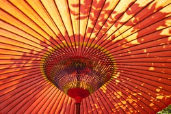 A closeup of a red, Japanese parasol from below with sun shining down