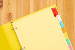 Blank file tabs in a yellow binder on wood desk mockup with copy space for your school or business message