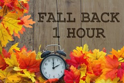 Fall Time Change, Autumn Leaves and Alarm Clock with grunge wood with text Fall Back 1 Hour