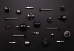 Studio photography - a lot of automotive parts: valves, spark plugs, silent blocks, thermostats, filter, sensors, ball bearings, lie in straight rows on a flat surface isolated on a black background.