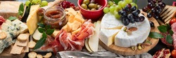 Appetizers table. Cheese, fuits and meat board on dark  background. Panorama banner