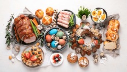 Traditional Easter dinner or  brunch with ham, colored eggs, hot cross buns, cake and vegetables. Easter meal dishes with holday decorations. Top view, flat lay