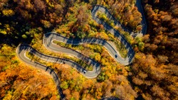 Aerial top drone view of winding forest road in the mountains. Colourful landscape with rural road, trees with yellow and green leaves.