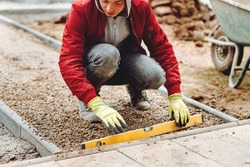Close up of construction worker installing and laying pavement stones on terrace, road or sidewalk. Worker using pavement slabs and level to build stone sidewalk
