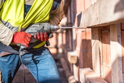 Worker using a drilling power tool on construction site and creating holes in bricks 