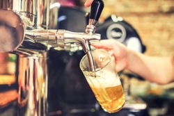 barman hand at beer tap pouring a draught lager beer serving in a restaurant or pub. Vintage soft effect on photo