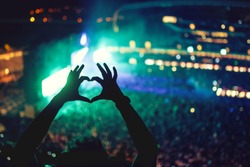 Heart shaped hands at concert, loving the artist and the festival. Music concert with lights and silhouette of a man enjoying the concert