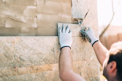 mason worker installing stone tiles on wall on construction site