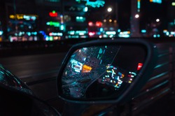 Abstract night city blurred background, colorful reflections and raindrops on wet car mirror