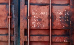 Old red shipping container door with technical characteristics text, background photo texture