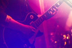 Electric guitar player on a stage with colorful blue and purple scenic illumination, soft selective focus