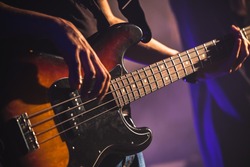 Close-up photo of bass guitar player hands, soft selective focus, live rock music theme