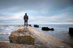 A man on the old broken pier starring at the restless Sea