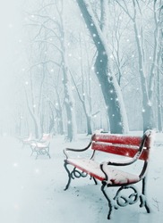 Row of red benches in the park in the snow in winter