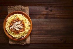 Spaghetti with homemade bolognese sauce made of fresh tomato, mincemeat, onion, garlic, carrot, served on wooden plate with grated cheese on top, photographed overhead on dark wood with natural light