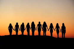 Sunrise silhouette of 10 young women walking hand in hand.