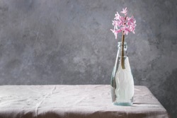 Spring blooming pink hyacinth in blue glass bottle standing on table with linen tablecloth.