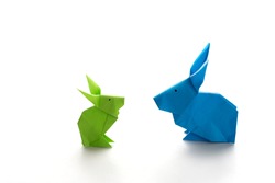 Two colorful origami Easter bunny rabbits made of paper in green and blue, of different sizes, perhaps parent and baby regarding each other, ready for Easter, isolated on white background