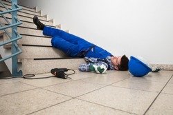 Unconscious Handyman Lying On Staircase With Helmet And Drill On Floor