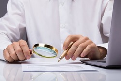 Midsection Of Businessman Examining Invoice With Magnifying Glass At Desk
