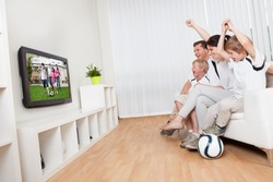 Young family watching football match at home