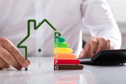 Close-up of a businessman using calculator holding outline of house model with energy efficiency rate