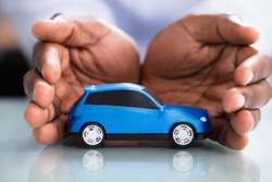 Businessman's Hand Protecting Blue Toy Car On The Reflective Desk