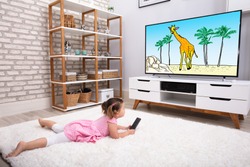 Rear View Of Innocent Girl Lying On Carpet Watching Cartoon On Television