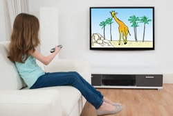 Side View Of Girl Sitting On Sofa Watching Cartoon On Television