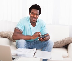 Happy African Young Man Calculating His Finance Expenses At Home