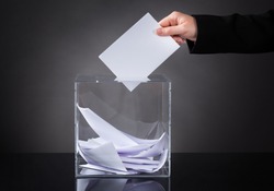 Close-up Of Hand Putting Ballot In Glass Box
