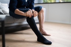Man Putting On Medical Compression Stockings On Legs