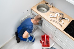 Male Plumber Cleaning Clogged Sink Pipe In Kitchen